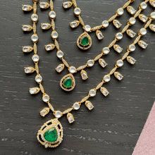 Load image into Gallery viewer, Gold necklace with emerald green stones on a dark surface