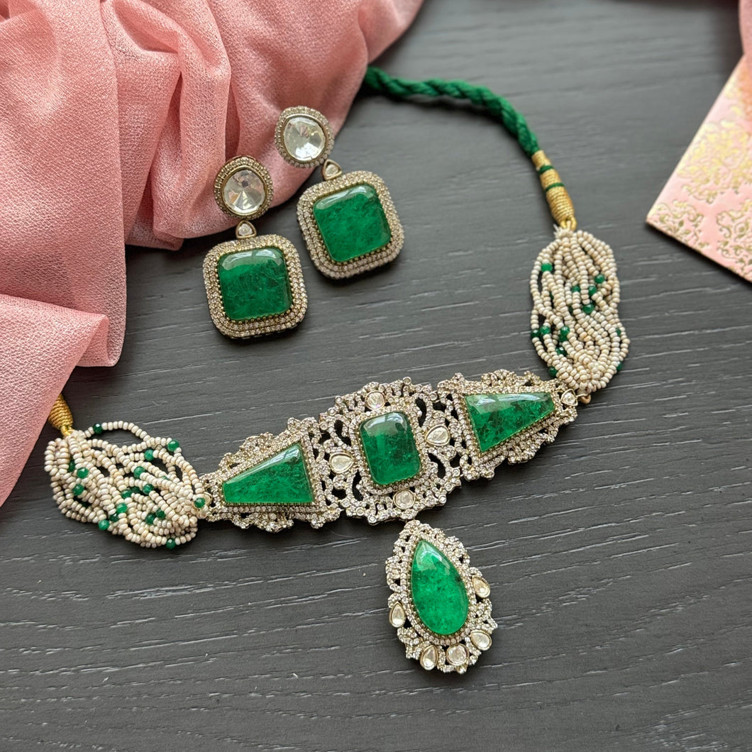 Jewelry set with green gemstones and gold accents on a dark surface with pink fabric.